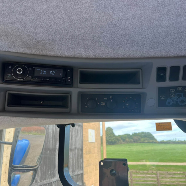 Cab dashboard with radio and climate controls, overhead console, and large side window showing a fence and field outside