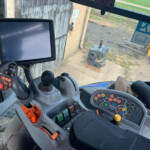 Inside the cabin of a heavy construction machine with a large screen monitor and multiple control joysticks and buttons.