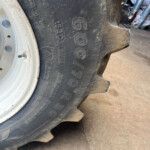 Close-up of a dusty tractor tire with a white wheel rim, showing large tread blocks and tire markings nearby.