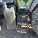 Close-up of a tractor cab with a metal stepped ladder, rusted steps, and large tires; Delta logo on the window and a Lincolnshire Motors sticker visible on the body.