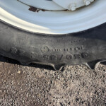 Close-up of a black car tire on a gravel surface, with a light gray wheel rim showing rust spots and bolts nearby.