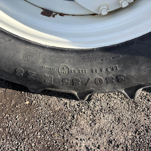 Close-up of a black car tire on a gravel surface, with a light gray wheel rim showing rust spots and bolts nearby.