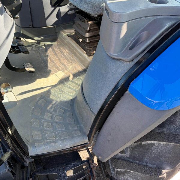 Interior of a blue vehicle cabin, showing pedals, a rugged rubber floor mat, and the driver area from an open door