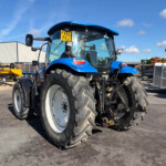 Blue tractor in an outdoor equipment yard with other machinery in the background and a clear blue sky.