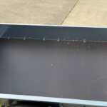 The interior of a loading trailer ramp with a textured black floor, riveted steel side panels, and diamond-plate edge against a concrete surface outside.