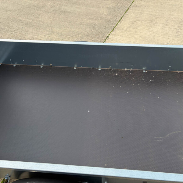 The interior of a loading trailer ramp with a textured black floor, riveted steel side panels, and diamond-plate edge against a concrete surface outside.