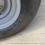 Close-up of a tire and steel wheel with lug nut visible and stamped tire size markings like 205/60R on the sidewall.