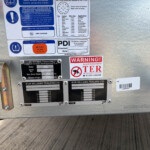 Close-up of a metal trailer door with multiple safety and weight labels, including tire pressure and warning stickers, plus a barcode plate.