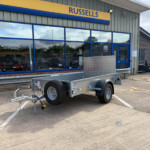 Storefront with a yellow-and-blue Russells sign and large blue-framed windows; a metal trailer sits in the parking area in front of the shop edge of road.
