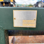 Close-up of a worn metal nameplate on green machinery with a ribbed belt below.