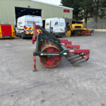 Industrial yard scene with two white Russell's vans near a green warehouse; foreground shows a red NRH Engineering roller/compactor piece of equipment.