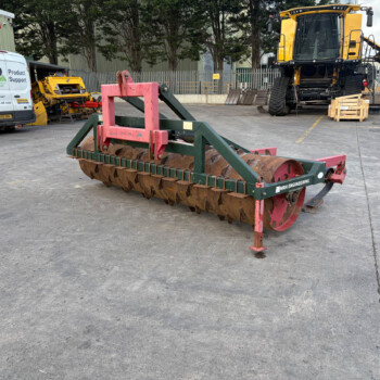Industrial equipment yard with a red-green soil roller in the foreground and a large yellow excavator in the background, plus a van on the left.
