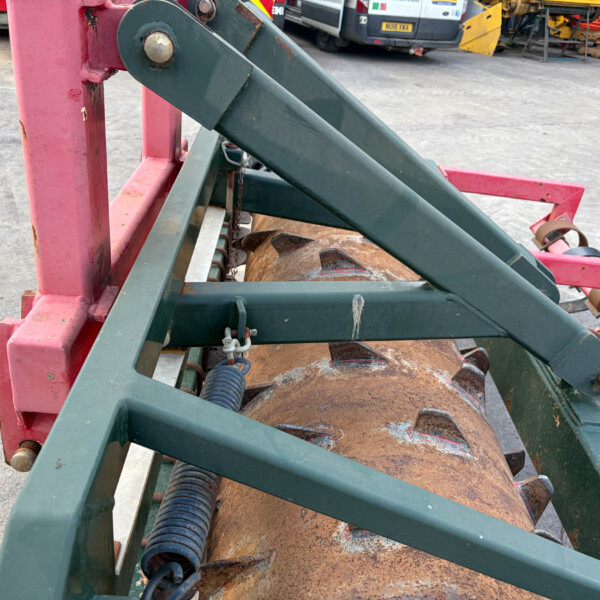 Close-up of green metal beams and a pink frame of a rusted agricultural implement in a yard.
