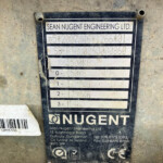 Metal identification plate on a dirty concrete surface reading Sean Nugent Engineering Ltd with weight and serial data