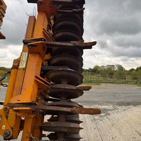 Orange heavy roller equipment with stacked steel drums for soil compaction on a road, overcast sky in background.