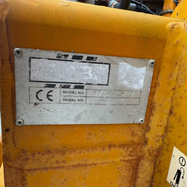 Close-up of a worn yellow metal machine frame with a rectangular metal plate showing model and serial information. The plate is dirty and scratched.