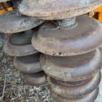 Close-up of rusted circular metal discs stacked together on orange machinery, with frayed rope tangled among them.