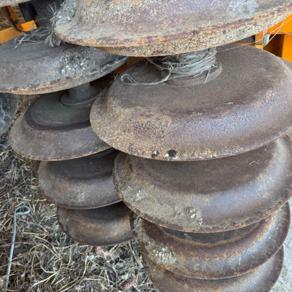 Close-up of rusted circular metal discs stacked together on orange machinery, with frayed rope tangled among them.