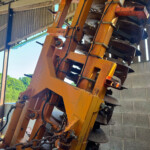 Close-up of orange industrial machinery with hoses and metal arms inside a shed, concrete block wall in the background.