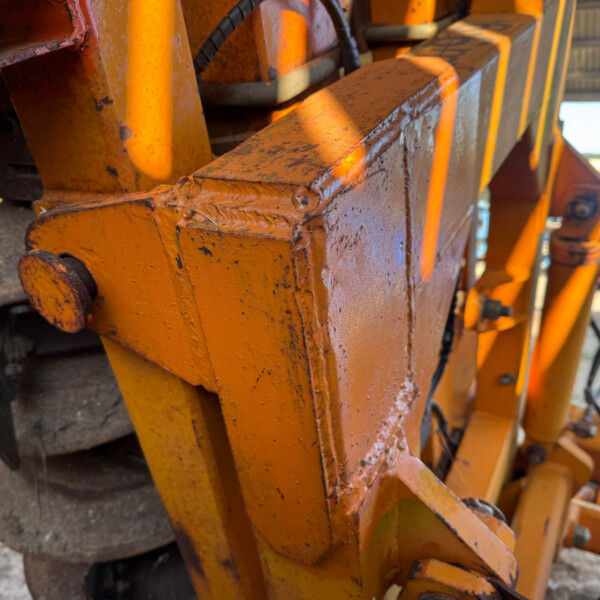 Close-up of orange industrial machinery frame showing worn paint, rust, and welded joints.