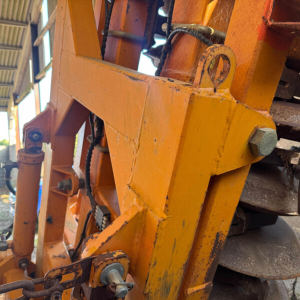 Close-up of orange metal framework with bolts, chains, and rust in an outdoor workshop area.