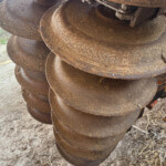 Stack of large rusted auger drill bits, stacked in a spiral outdoors