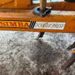 Close-up of an orange Simba Double Press machine, showing a rusted bolt and worn label on the frame