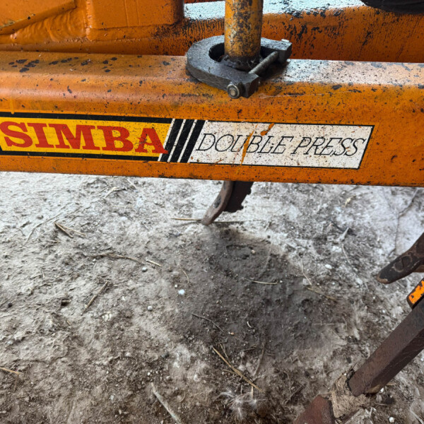 Close-up of an orange Simba Double Press machine, showing a rusted bolt and worn label on the frame