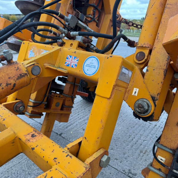 Close-up of yellow heavy-duty hydraulic construction equipment with black hoses, metal fittings, and bolts, showing wear and rust.