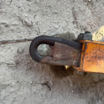 Cracked, dry soil with small rocks, and part of an orange and black metal tool in the bottom-right corner.