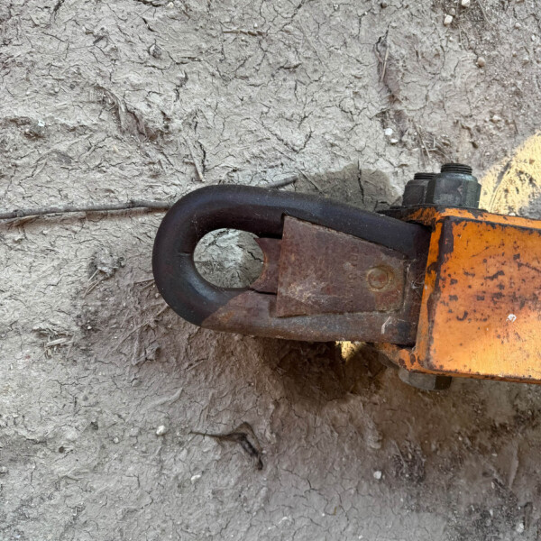 Cracked, dry soil with small rocks, and part of an orange and black metal tool in the bottom-right corner.