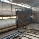 Interior of a dusty, rusted metal trailer with blue support beams and a diamond-plate floor, covered in grime and dirt.