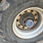 Close-up of a dusty, worn tire with a rusting white wheel and bolts visible at the hub.