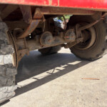 Underside of a large, red dump truck showing rusted axles, suspension components, and a big off-road tire.