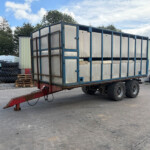 Large blue-framed trailer with aluminum panels sits in an industrial yard, nearby tires, pallets and equipment visible.