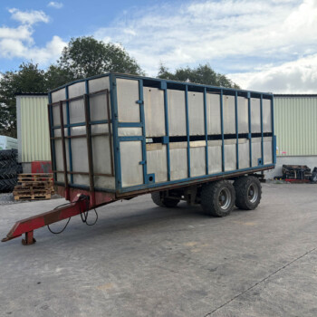 Large metal trailer on a wheeled platform in an industrial yard, with stacked tires and pallets nearby.
