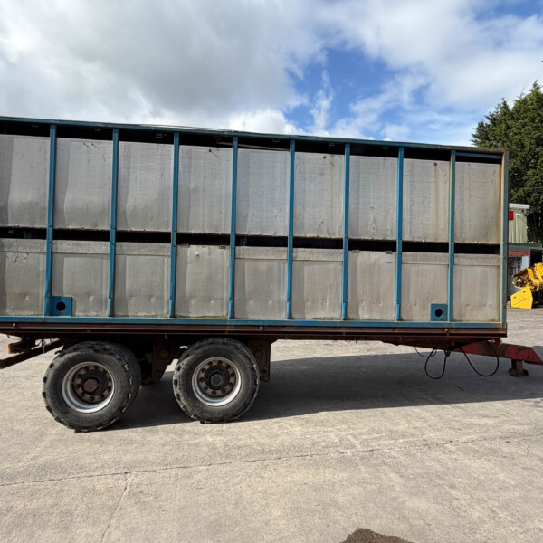 Blue-framed metal trailer with vertical ribs and gray panels, parked on an asphalt lot under a cloudy sky in an industrial yard.