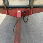 Close-up of a rusty red trailer frame with hoses and a hitch on a concrete surface.
