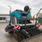 Large blue farming implement with rotating disk harrows on a trailer in a workshop yard, secured for transport from Russells.