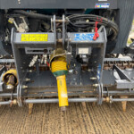 Close-up of the machine's rear drive area with bundled hydraulic hoses, metal brackets, and a yellow PTO shaft