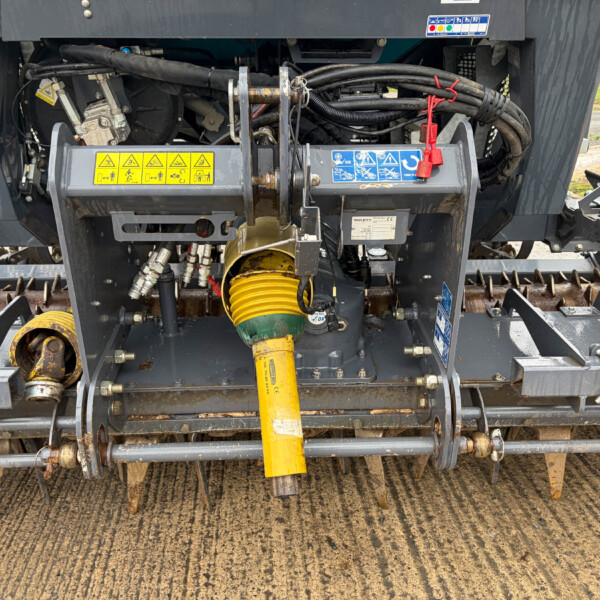Close-up of the machine's rear drive area with bundled hydraulic hoses, metal brackets, and a yellow PTO shaft