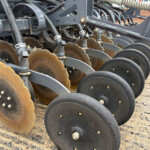 Close-up of rusted disc blades on a farming harrow, arranged in a row on a metal frame.