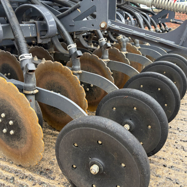 Close-up of rusted disc blades on a farming harrow, arranged in a row on a metal frame.