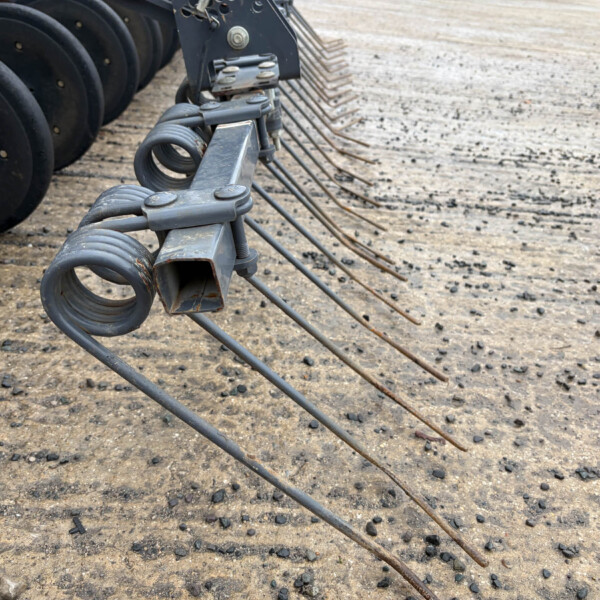 Close-up of a farm or construction implement with curved tines and a gray metal frame on a dirt surface at a work site