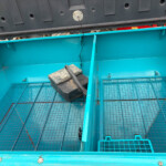 Open teal dumpster interior with a wire-mesh floor and a black toolbox resting inside near the divider.