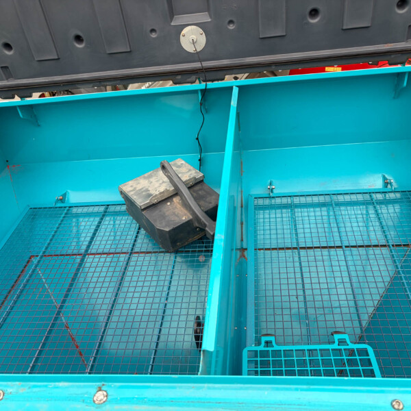 Open teal dumpster interior with a wire-mesh floor and a black toolbox resting inside near the divider.