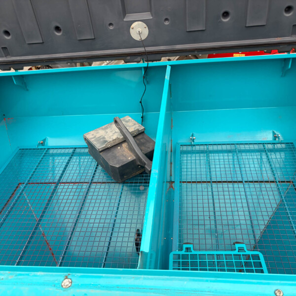 Open turquoise truck bed with a wire-grid floor, a black toolbox resting near the center, and straps hanging from the sides inside the cargo area.