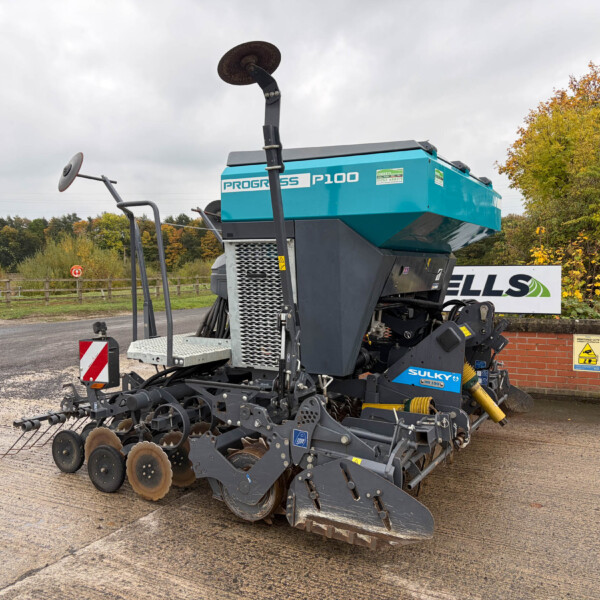 Progress P100 teal and gray agricultural harvester parked outdoors in a yard, with autumn trees in the background.