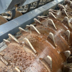 Close-up of rusted, jagged metal blades from agricultural equipment with grime and dirt buildup.