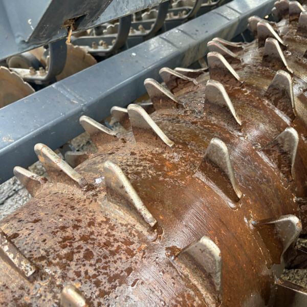 Close-up of rusted, jagged metal blades from agricultural equipment with grime and dirt buildup.